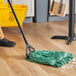 A person cleaning a floor with a Lavex Pro green rayon blend mop and bucket.