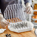 A person in gloves holding a plastic container with Ateco pastry tip compartments.