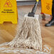 A person mops the floor with a Choice natural cotton mop head.