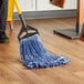 A person using a Lavex blue looped end mop to clean a wood floor.