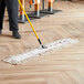 A person using a Lavex white cotton dry dust mop to clean a floor.