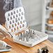 A person holding a white plastic container with silver Ateco pastry tips in a plastic tray.