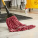 A person in a yellow room using a Lavex Pro red rayon blend mop head with a yellow handle to clean the floor.