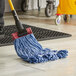 A person using a Lavex Blue Cotton Mop with a yellow mop bucket to clean the floor.