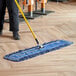 A person mopping a floor with a blue Lavex dry dust mop.