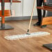 A Lavex white cotton dry dust mop head on a wood floor.