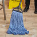 A person mopping a tile floor with a blue Lavex cotton blend mop.