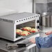 A person using a spatula to cook food in an Avantco electric countertop cheese melter.