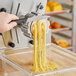 A person using a black-handled machine to cut Capellini pasta.