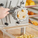 A hand with a black and yellow tool using a machine to cut dough.