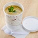 A Solo Symphony paper soup cup filled with soup and a white lid with a spoon on the side.