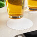 A close-up of a glass of beer on a Hoffmaster white round coaster.