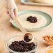 A Tablecraft beige polycarbonate perforated portion spoon with beans in it being held over a bowl of beans.