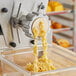 A yellow pasta machine die extruding Mafaldine pasta.