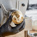 A person in black gloves using a gold Estella penne pasta die to grind a metal object on a counter.