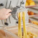 A hand using a yellow and white handle to cut pasta with a round yellow #38 Pappardelle pasta die.