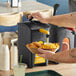 A hand pouring ServSense honey mustard into a container of chicken nuggets using a ServSense condiment pump with a yellow label.