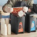 A person in a black apron using a ServSense BBQ pouch dispenser to fill a black container with red sauce.