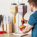 A man using an Asept hanging condiment pump to pour ketchup onto a burger.