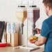 A man using an Asept hanging bottle pump to dispense condiments over a basket of food.