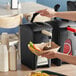 A person using a black ServSense mayonnaise pump to pour liquid onto a sandwich.