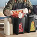 A person using a ServSense plastic ketchup pouch dispenser to fill a white cup.