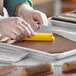 A person in gloves using a yellow rubber spatula to cut chocolate in a Pavoni Pavoflex silicone baking mold.