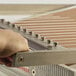 A hand using a Pavoni candy slicer to cut candy on a metal surface.