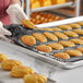 A person holding a black Pavoni Pavoflex silicone baking mold filled with Madeleine cakes.