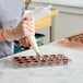 A woman using a pastry bag to fill a Pavoni hexagon candy mold with chocolate.