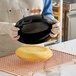 A person using a black Pavoni Pavocake baking mold to make a round cake.