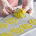 A person in gloves using a Pavoni honeycomb baking mold to make yellow hexagon-shaped cookies.