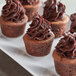A group of mini chocolate muffins with chocolate frosting on a white plate.