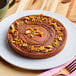 A Pavoni stainless steel micro-perforated tart ring with a chocolate cake with nuts on top on a plate with a fork.