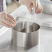 A person wearing gloves and holding a PVC Cake Collar roll over a metal container.