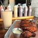 A black giant straw placed in a glass of milkshake next to a tray of chicken wings and dipping sauces.