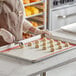 A woman wearing an apron uses a Pavoni silicone baking mat to prepare cookies on a baking sheet.