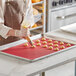 A person in an apron using a Pavoni silicone mat to pipe dough for pastries.