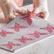 A person in gloves using a Pavoni Gourmand butterfly baking mold to cut a pink butterfly shape.