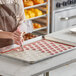 A person in a kitchen using a Pavoni full size macaron baking mat to bake pink cookies.