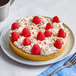 A tart with whipped cream and raspberries on a plate with a fork.