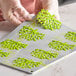 A person's hand holding a Pavoni Gourmand coral silicone baking mold filled with green batter.