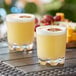 Two Acopa Endure Tritan plastic rocks glasses filled with yellow liquid and orange slices on a table.