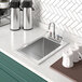 A Regency stainless steel drop-in sink with a swivel faucet next to a white coffee mug.