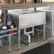 A Regency stainless steel underbar sink with left drainboard on a counter with bottles of liquid in it.