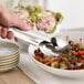 A hand using Acopa stainless steel tongs to serve food from a bowl.