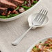 An Acopa stainless steel serving fork next to a plate of food