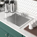 A Regency stainless steel drop-in sink with a faucet in the middle and coffee mugs and containers above it.