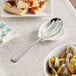 An Acopa stainless steel slotted serving spoon on a plate with food.