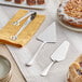 A table with Acopa stainless steel serving utensils and a cake server on a white surface.